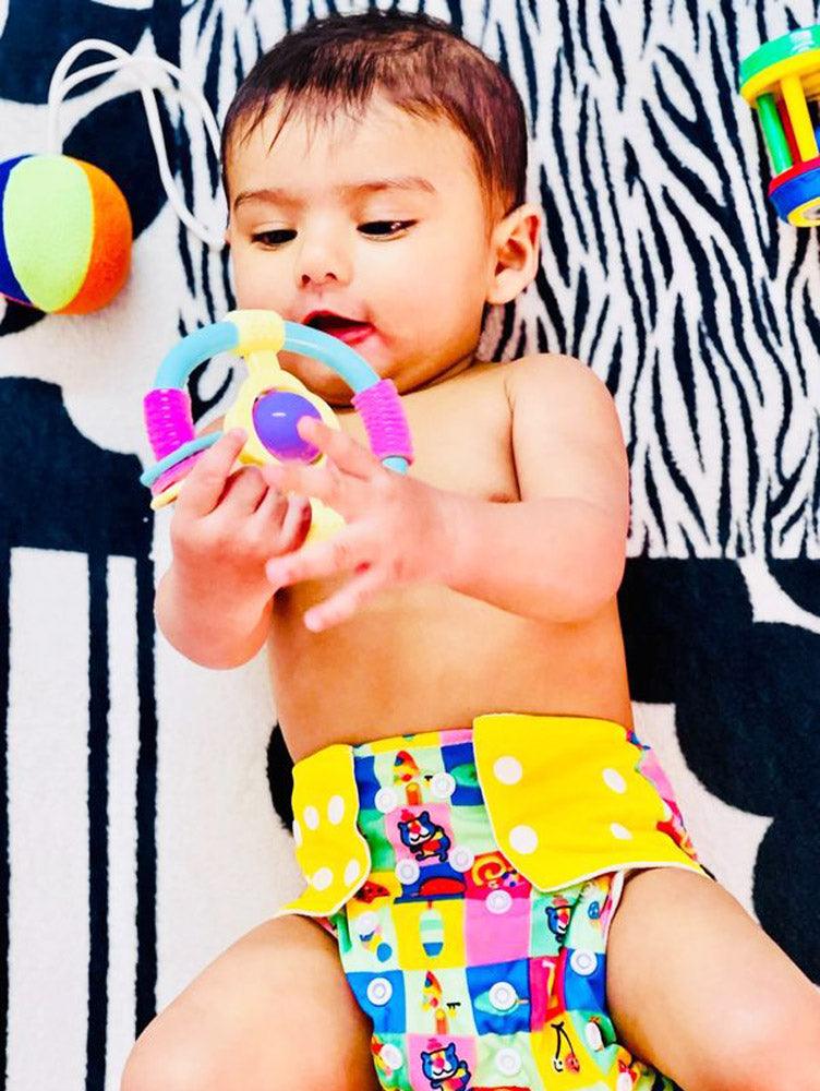 baby wearing yellow cloth diaper playing with toys