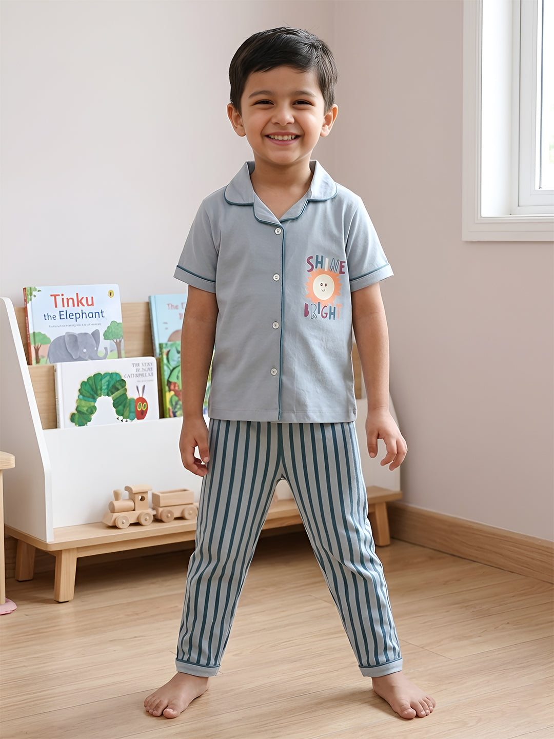 Child wearing a light blue pajama set with striped pants in a room with books and toys.