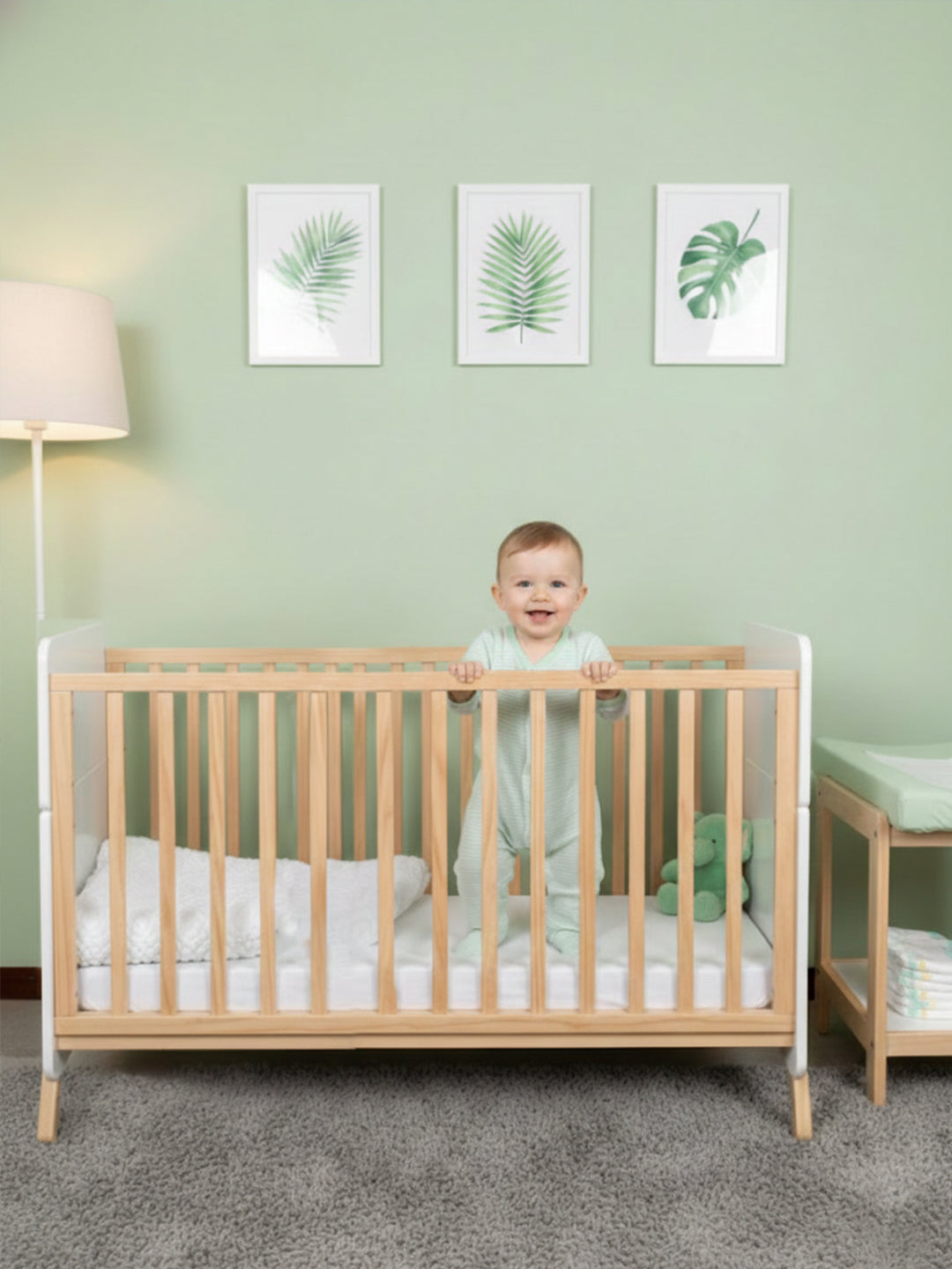 Baby standing in a crib with a green wall and plant decorations