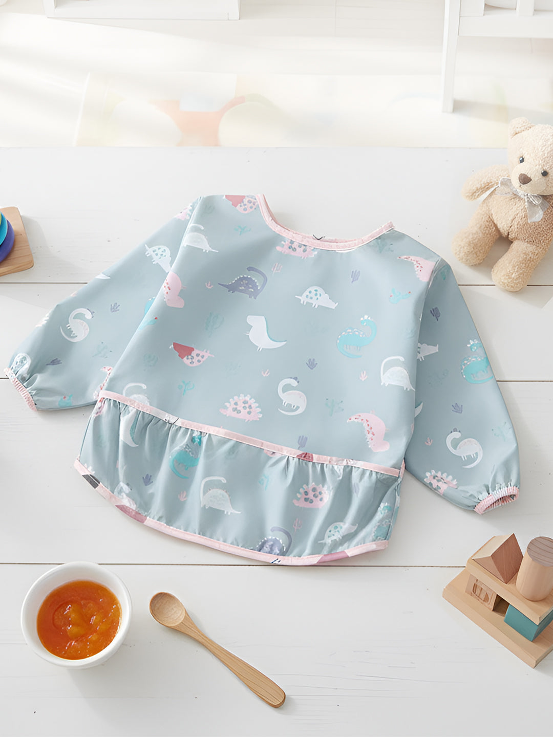 Baby bib with animal pattern on a white surface with toys and a bowl of food.
