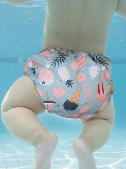 Baby wearing a colorful swim diaper with ice cream and floral pattern underwater.