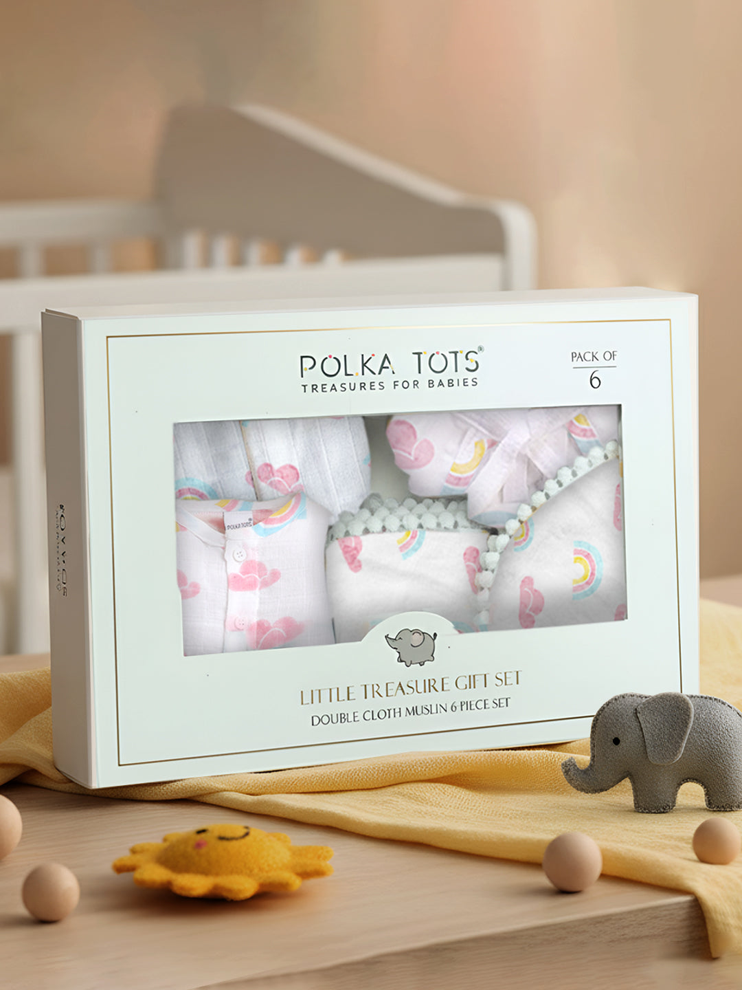 Polka Tots baby gift set packaging on a wooden surface with toys and a crib in the background