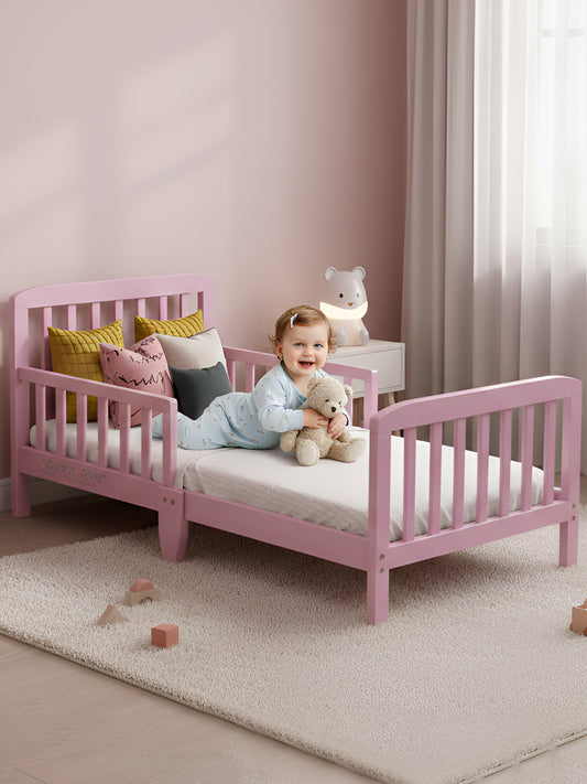 Child on a pink toddler bed in a room with light pink walls and a white curtain.