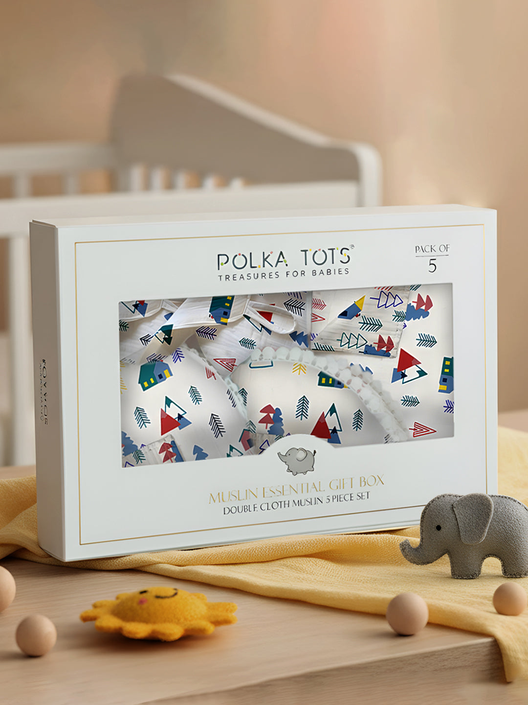 Polka Tots baby muslin essential gift box with baby toys on a wooden surface