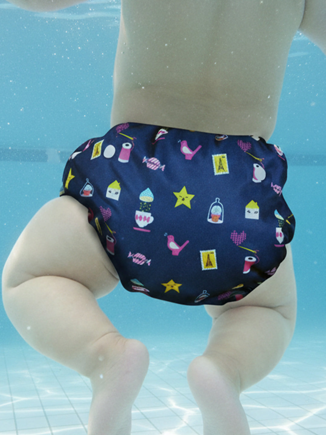 Navy swim diaper with colorful patterns on a doll against a pool background