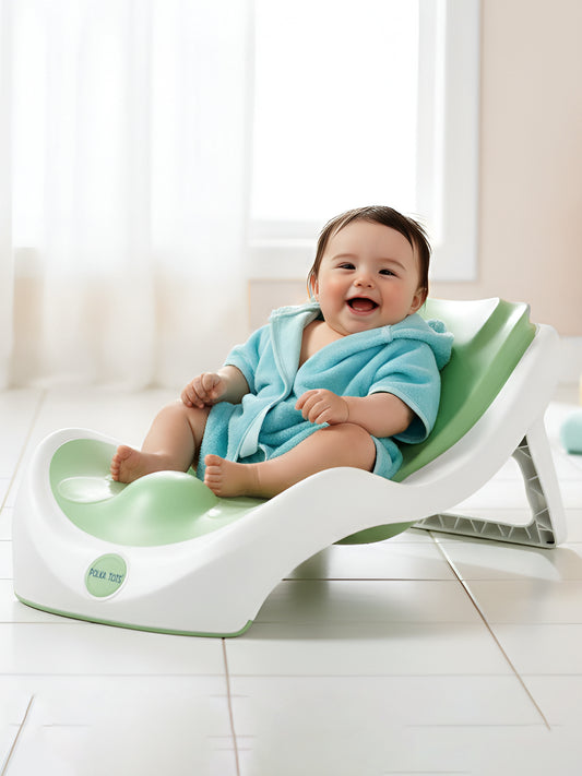 Baby in a blue bathrobe sitting on a green and white baby seat with a white curtain in the background.