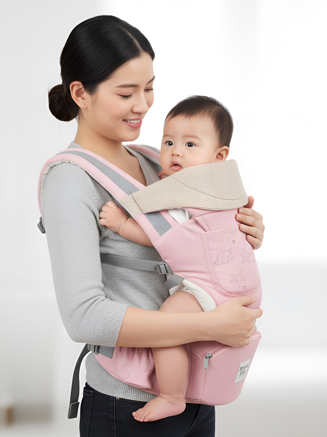 Woman holding a baby in a pink and gray baby carrier against a white background