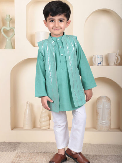 Young boy wearing a green kurta with white pants in a decorative setting.