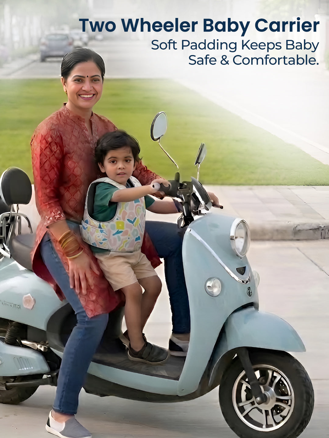 Woman and child on a scooter with a two-wheeler baby carrier, set against a road and grass background.