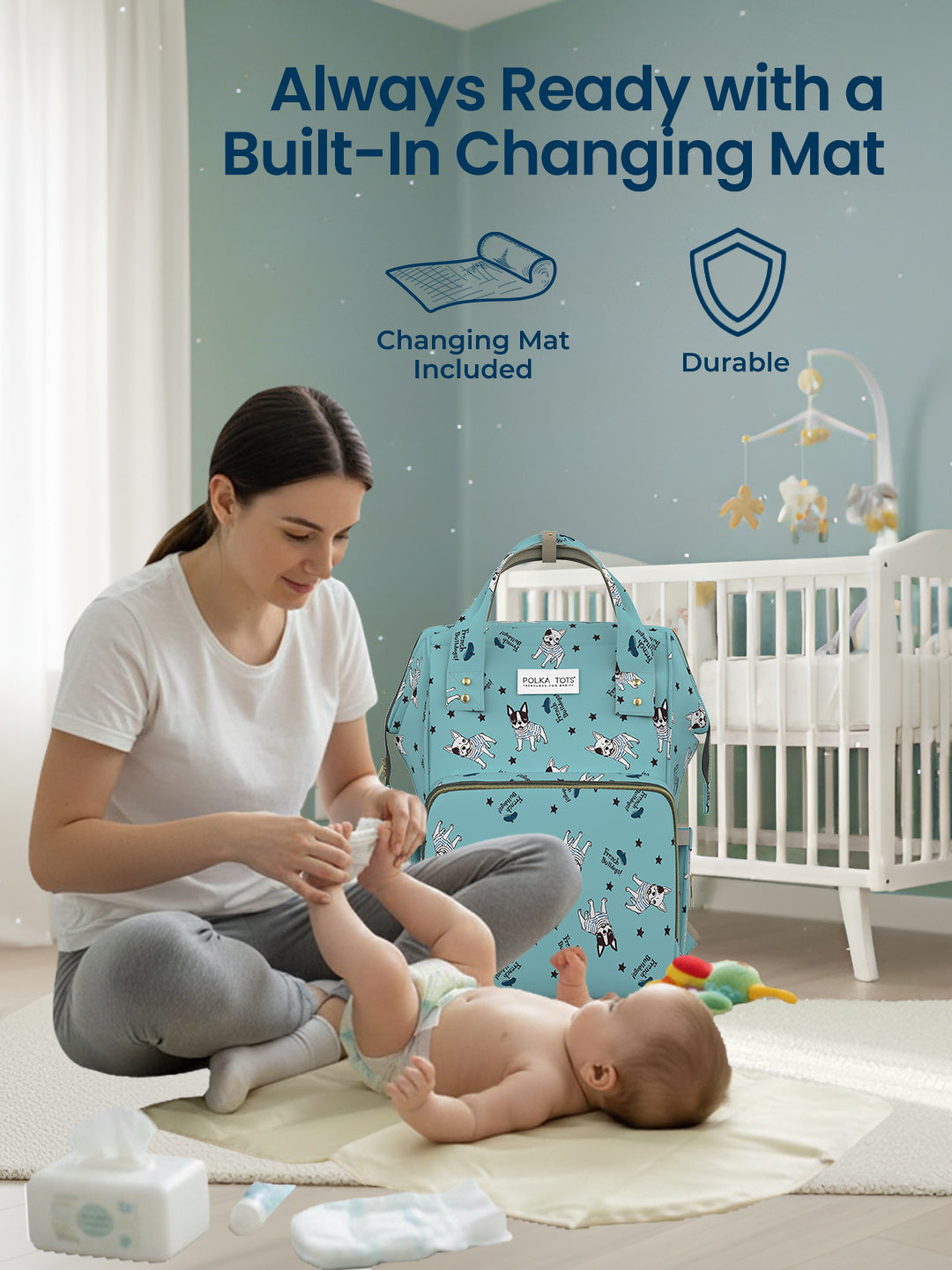 Woman changing a baby on a changing mat with a blue diaper bag in the background.