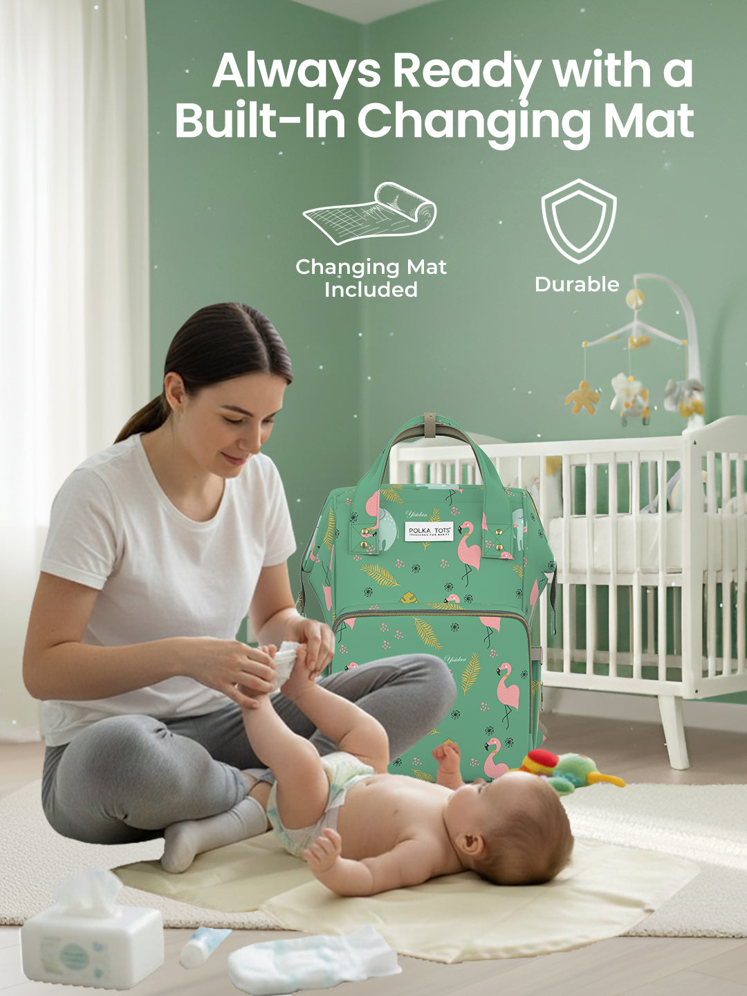 Woman changing a baby on a changing mat with a green bag labeled 'Always Ready with a Built-In Changing Mat' in the background.