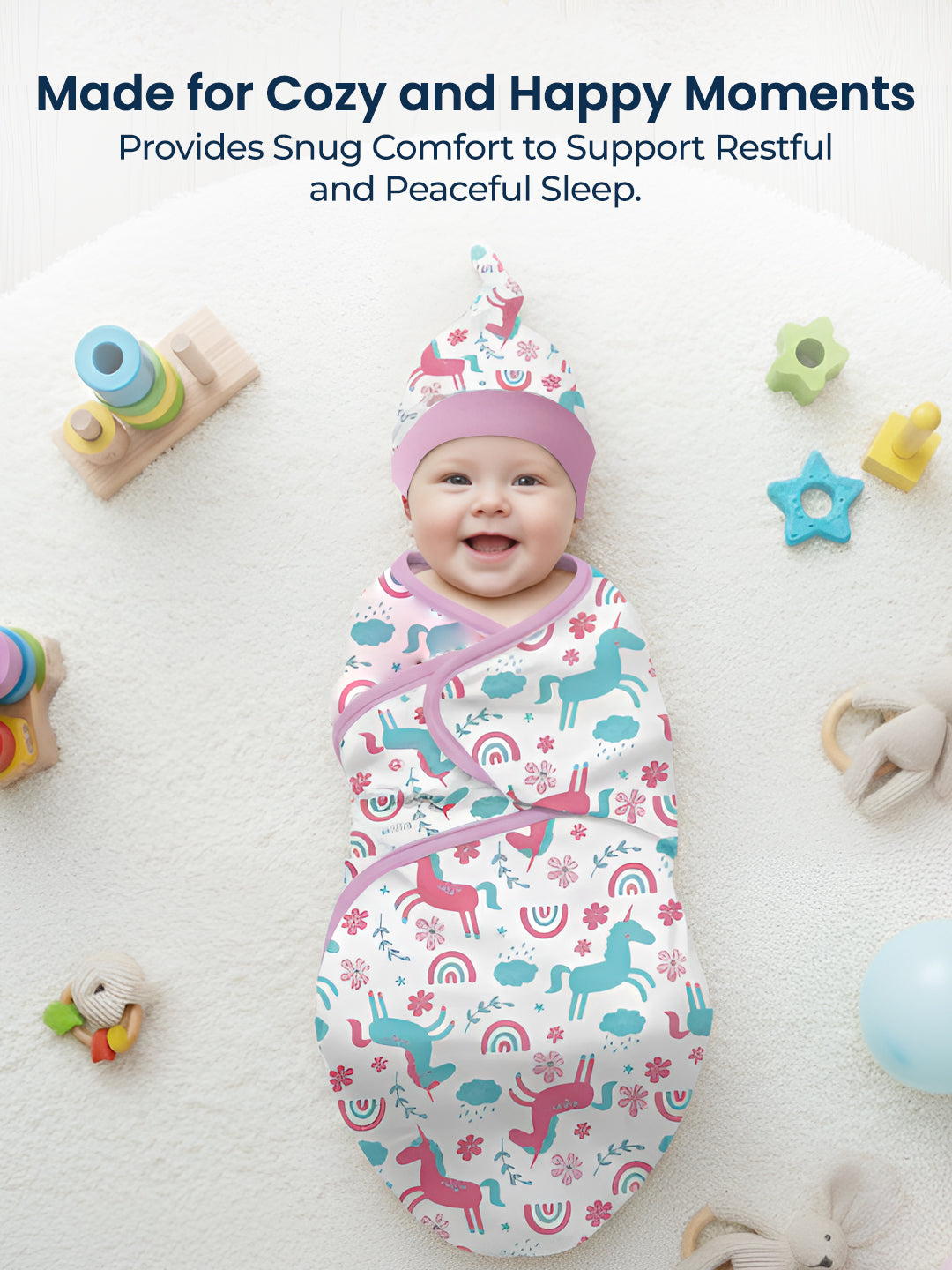 Baby swaddled in a colorful blanket with unicorn pattern, surrounded by toys on a white background.