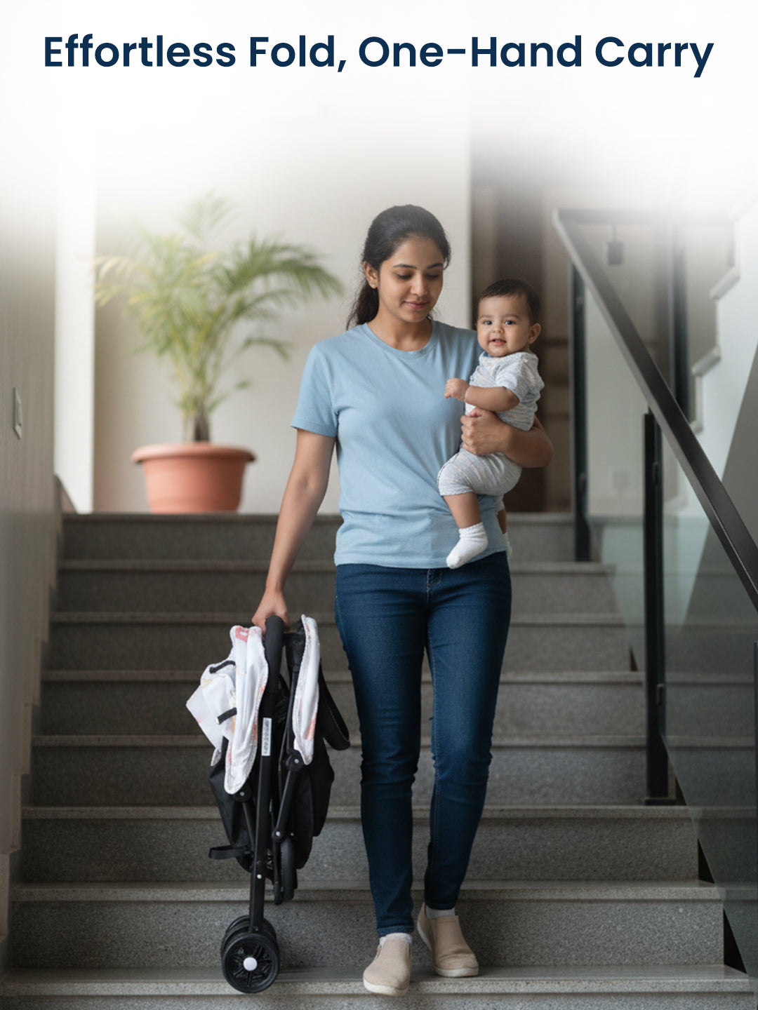 Woman holding a baby and a folded stroller on a staircase