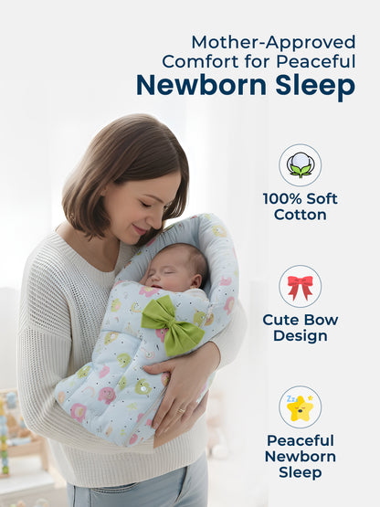 Woman holding a baby wrapped in a soft, white blanket with a green bow, set against a light background.