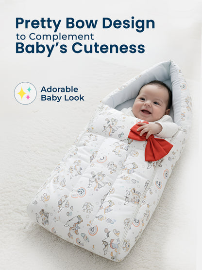 Baby wrapped in a white blanket with a red bow, sitting on a light gray surface.