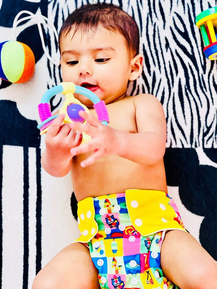 baby wearing  yellow cloth diaper playing with toys 